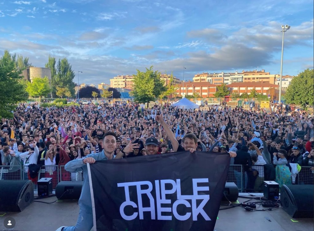 Triple Check: outdoor stage, band holding TRIPLE CHECK banner, large crowd